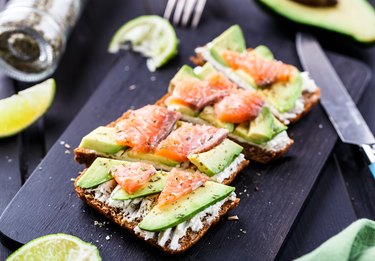 Sandwich with avocado and smoked salmon on black wooden cutting board with lime on side