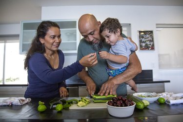 Two parents and a baby cutting vegetables in the kitchen
