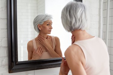 older woman looking at her dry skin in the bathroom mirror