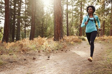 Person wearing blue long sleeve shirt and black leggings running an ultramarathon on a trail