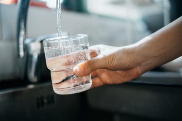 Close up of a person filling a clear glass with water from their kitchen sink