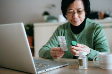 Senior Asian woman video conferencing with laptop to connect with her family doctor, consulting about medicine during self isolation at home in Covid-19 health crisis