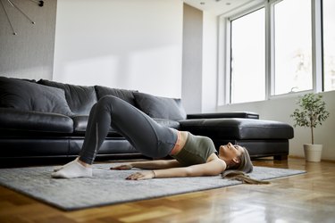 Person doing glute bridge as example of exercise to prevent IT band pain in living room on gray rug beside black leather couch.