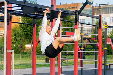 A man performs a leg raise on the bar in the morning on the sports field.