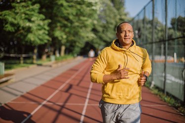 Person wearing a yellow sweatshirt and gray shorts running on a track to build leg muscle