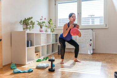 woman doing a goblet squat with a pink kettlebell in her living room