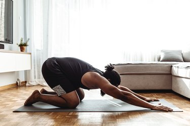 Person doing child's pose on yoga mat in living room