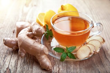 Cup of fresh ginger tea with lemon and mint next to ginger root on a wooden table.