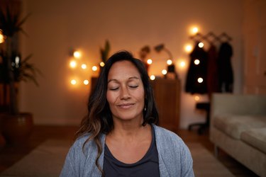 woman smiling while meditating at home, as a natural remedy for anxiety