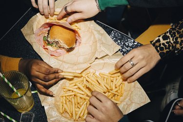 High angle view of friends eating fast food burger and french fries at table in cafe