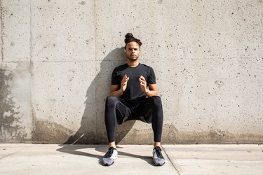 Young person with dreads doing a wall sit exercise as a leg press alternative