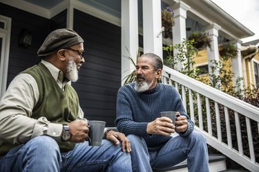 Two old bearded men drinking coffee while sitting on the steps in front of their house