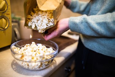 person pouring microwavable popcorn out of the packet and into a glass bowl
