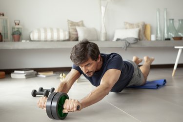 person wearing T-shirt and shorts exercising in living room with an ab roller