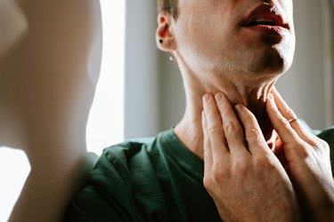 Close up of a person touching their throat, feeling throat pain after throwing up