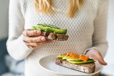 Close up of woman holding plate with avocado toast, as an example of good foods for breastfeeding