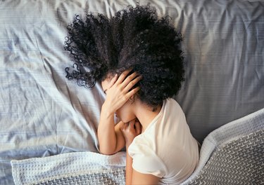 overhead shot of woman in bed covering ear