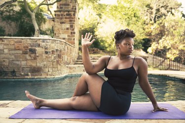 Confident woman doing spinal twist on mat at poolside