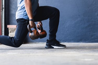 close up picture of a man doing a lunge with kettlebells