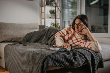 Woman reading a book on the couch, as an example of how to treat pink eye at home