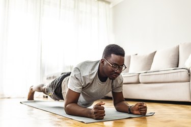 Adult male workout in his living room on yoga mat exercising plank position