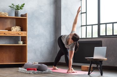 Person wearing gray athletic clothes in revolved triangle pose as an example of the best yoga poses for acid reflux.