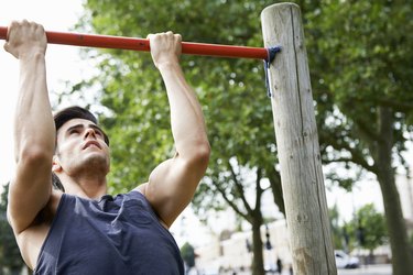man doing chin-ups and arm exercises in the park