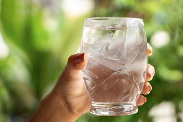A hand holding glass of ice water, one of the best home remedies for dry