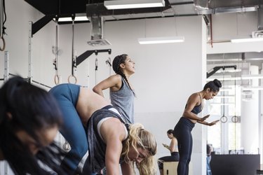 Group of exercises with ponytails and braids doing burpees in a gym during a workout class, while one person skips the move