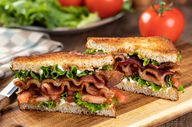 Vegan bacon, lettuce and tomato sandwich cut in half on wooden board