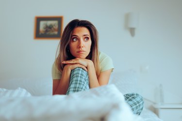 A person sitting on a bed in their pajamas looking anxious because they have the sunday scaries