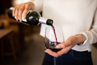 closeup of woman's hands pouring bottle of red wine into a glass