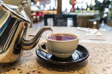 Silver teapot pouring herbal tea into white mug on restaurant table is one of the 15 foods to help GERD