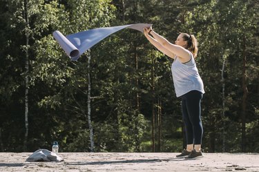 caucasian plus sized woman placing a yoga mat outside in front of a forest