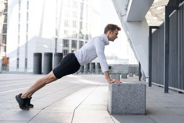 Person in workout clothes doing an incline push-up on a box outdoors