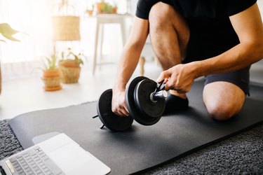 Young sporty man having sports training with dumbbells at home