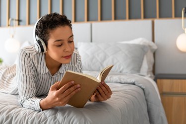 Woman listening to music and reading book on bed