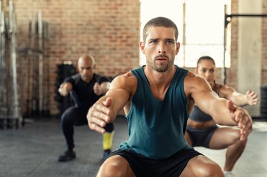 man squatting at a group fitness class, looking concerned about farting while working out