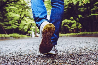 rear close up of a person's feet walking on a gravel road in a park with lots of green trees