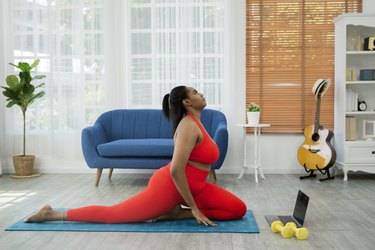 Person exercising at home on blue yoga mat with laptop following online workout program