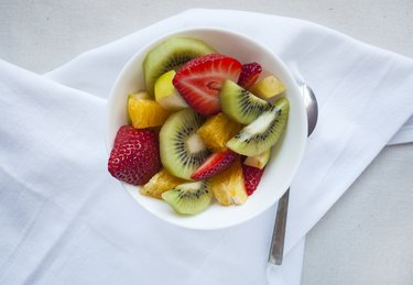 overhead photo of fresh fruit salad with strawberries and kiwi.on white napkin with silver spoon