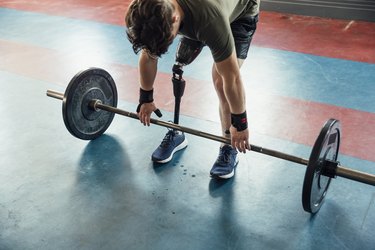 Person with prosthetic leg getting ready to lift a barbell in gym.