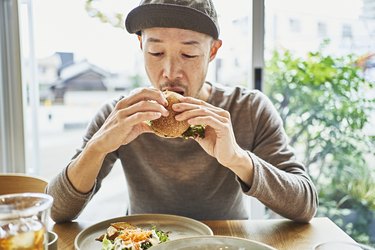 Asian man eating a veggie burger at a cafe