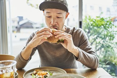 一名亚洲男子在咖啡馆吃素食汉堡