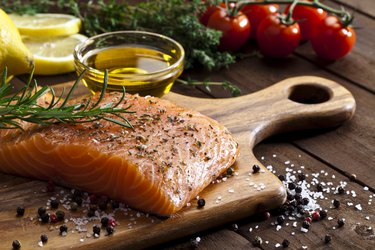 Raw salmon steak on wooden board with oil and veggies