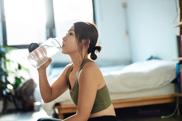 A person drinking from a bottle of water in their bedroom before their physical at the doctor
