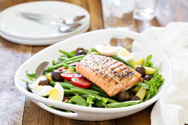 Grilled salmon nicoise salad on a white plate on a wooden table