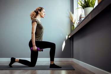 person performing reverse lunges on yoga mat at home holding two purple dumbbells