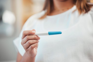 an unrecognizable person holding a pregnancy test and wondering if you can get pregnant on your period