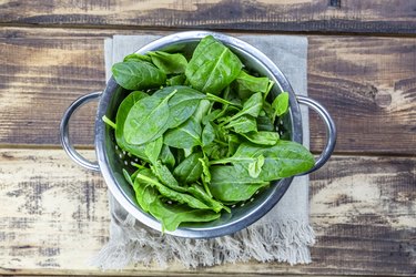 Fresh spinach leaves in colander on wood table are one of the best foods to lower blood pressure